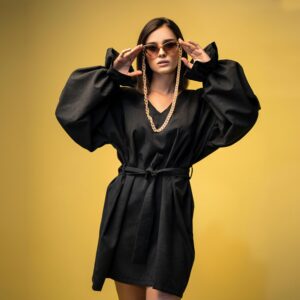 Stylish woman wearing a black dress and sunglasses against a yellow background.